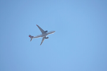 Airplane flying in the clear blue sky, bottom view. Commercial plane taking off and gaining altitude