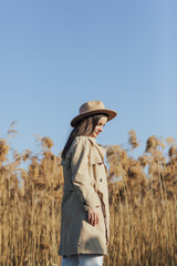 Beautiful woman in a hat and dressed in stylish clothes on a background of reeds and blue sky.