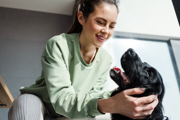 Smiling young brunette woman petting her dog at home