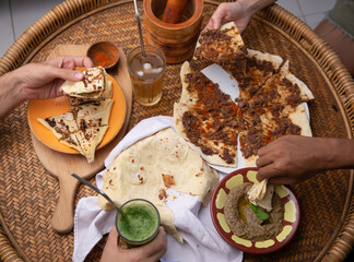Close up of hands taking Middle eastern or arabic dishes and assorted meze: hummus, pita, Manakish...