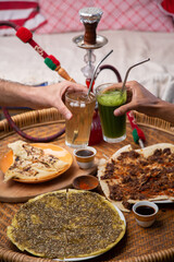 Fototapeta na wymiar Close up of people's hands cheering drinks over table with Middle eastern or arabic dishes, assorted meze and hookah
