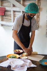 Man chef wearing face mask and preparing, wrapping traditional shawarma or gyro with meat, vegetables and sauces during pandemic