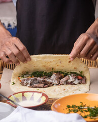 Men's hands preparing and wrapping traditional shawarma wrap or gyro with meat, vegetables and sauces