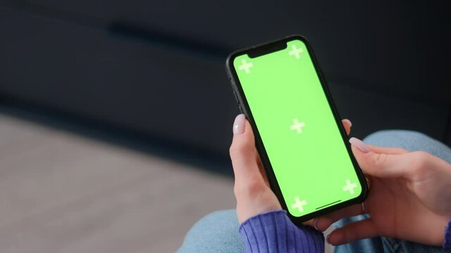 Young woman sitting on armchair at home and uses smartphone with green screen Mock-up. 4k	
