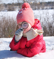 Little girl in warm winter clothes with a magnifying glass in her hand investigate  details of...