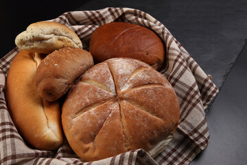 Freshly baked bread loaf bun roll round long mix verity wrapped in checkered kitchen fabric napkin towel over black background