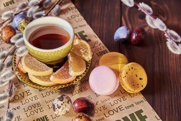 A ceramic green cup of tea, various sweets , willow branches and painted eggs on a paper napkin with the inscription love. Easter card.