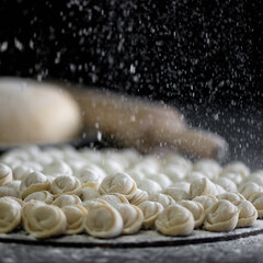 Flouring of uncooked ravioli or dumplings. Cooking process on black background. Close up shot. Soft focus in foreground. 