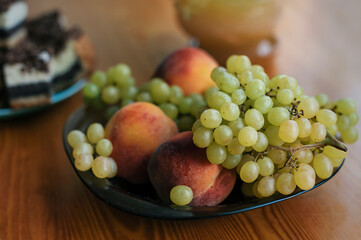 Fresh fruits on a plate. Green grapes and peaches. Healthy food on the kitchen table.