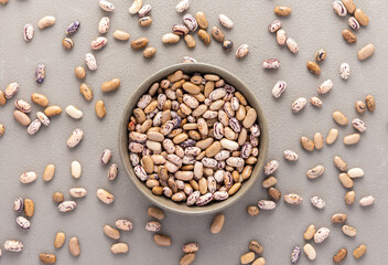 Legumes in bowl and scattered in the background, Pinto beans in a plate on a gray background, top view