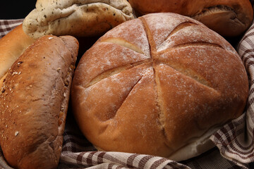 Freshly baked bread loaf bun roll round long mix verity wrapped in checkered kitchen fabric napkin towel over black background