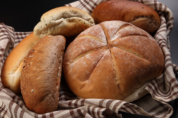 Freshly baked bread loaf bun roll round long mix verity wrapped in checkered kitchen fabric napkin towel over black background