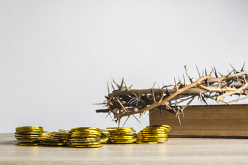 Coins on a wooden table with thorn crown and bible on a wooden background