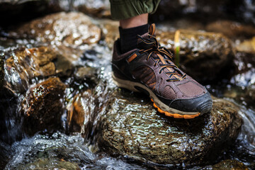 a foot in a brown trekking boot stands on a wet rock in a mountain river