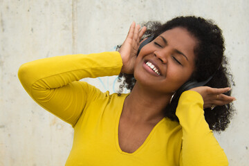 African american woman with afro hair and yellow t-shirt and bluetooth headphones dancing happily.