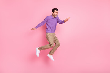 Fototapeta na wymiar Photo of positive cute young guy wear violet sweater jumping high looking empty space isolated pink color background