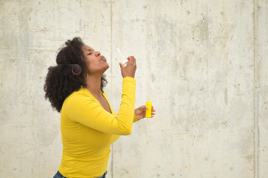 African american woman with afro hair and yellow t-shirt blowing soap bubbles.