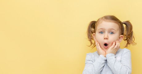 Wow. Closeup portrait of excited child touching her cheeks, over pastel yellow isolated...