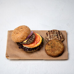 Grilled double or triple meat burger with tomatoes, onion and lettuce on parchment paper. Set of ingredients for super nutritious snack or lunch. Fast food, unhealthy eating concept. Top view.