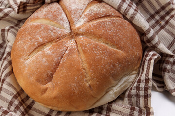 Fresh baked round bread loaf wrapped in checkered kitchen fabric napkin towel over white background