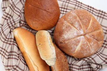 Freshly baked bread loaf bun roll round long mix verity wrapped in checkered kitchen fabric napkin towel over white background