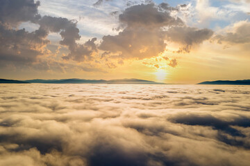 Aerial view of yellow sunset over white puffy clouds with distant mountains on horizon.