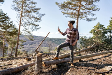 Lumberjack man making photo with mobile phone next to cut log and his ax