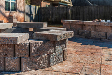 Incomplete paver patio hardscape with a stone fire pit and seating wall under construction in a...