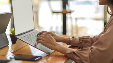 Female hands typing on laptop keyboard on wooden desk in office room