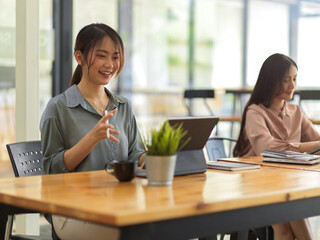 Female office worker smiling and talking while working with digital tablet in office room