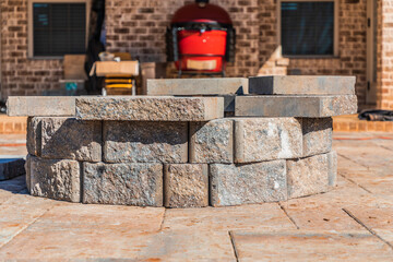 Incomplete paver patio hardscape with a fire pit feature under construction in a suburban backyard