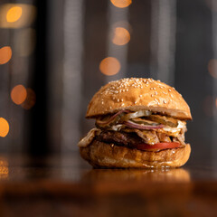 Classic American meat hamburger with onions and tomatoes on wooden table. Beautiful bokeh lights on...