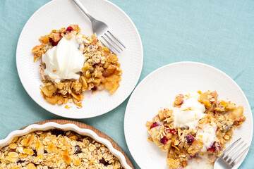 Two plate with apple pear crumble with ice cream, streusel. Sweet dessert with stewed fruit topped crisp crumbly mixture served ice cream. Apple cobbler pie in baking dish on tablecloth. Top view
