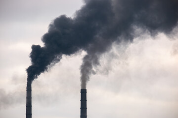 Coal power plant high pipes with black smoke moving up polluting atmosphere.