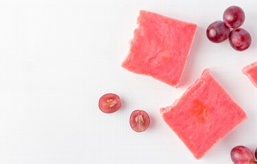Pink bars of soap with red grape seed extract on a white wooden background with empty space. Healthy essential cosmetics for body care, top view.