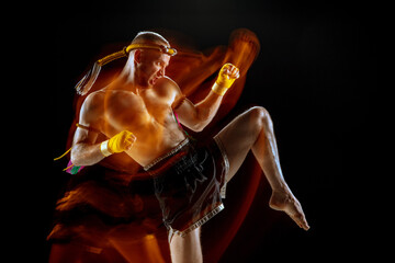 Young man thai boxer training over dark background in neon mixed light.