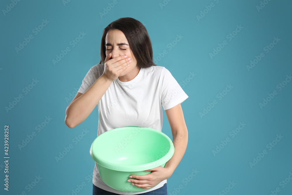 Poster Young woman with basin suffering from nausea on light blue background. Food poisoning