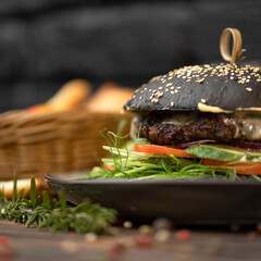 Black burger made from rye bun, juicy meat and herbs on plate. Fast food menu concept. Nutritious snack or lunch. Classic American food. Close up shot with soft focus. Side view.