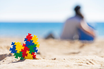 Puzzle heart on the sand and silhouette of mother hugging the child on the beach and looking to the sea ocean. Autism awareness day concept