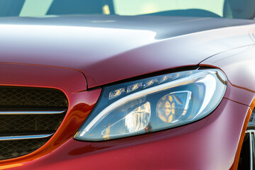 Closeup of front headlight of new clean car parked on a city street side.