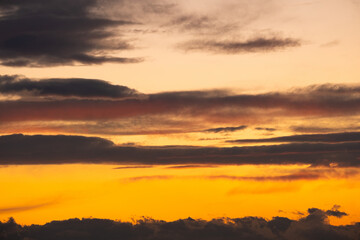 Dramatic sunset landscape with puffy clouds lit by orange setting sun and blue sky.