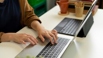 Female hand typing on laptop keyboard on office desk with another laptop, books and stationery