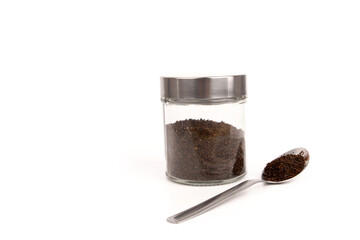 A top view of blended and dried tea leaf in a glass jar and on a spoon isolated on white background