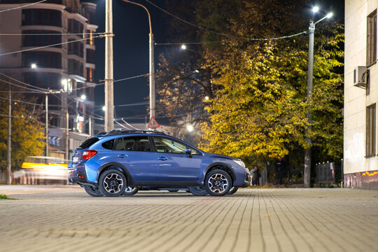 Blue car parked on brightly illuminated city street at night.