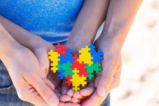 Autistic kid hands supported by mother holding multicolored puzzle heart. World autism awareness day concept