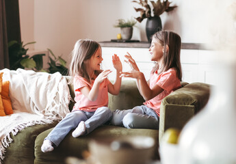 Two little girls sisters play fun on the couch in the living room. Children happily spend time...