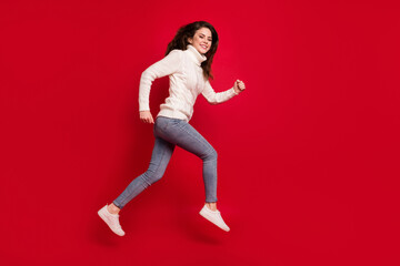 Full length photo of pretty sweet young woman dressed white sweater running fast jumping high isolated red color background