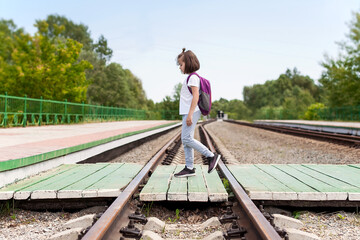 Crossing the railway tracks made of wood across the railway tracks  in the daytime. Schoolgirl  carrying scooter and crossing road. Pedestrian passing a crosswalk. Safety  concept for road users