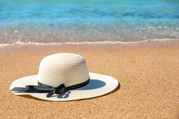 Fototapeta na wymiar White woman straw hat laying on tropical sand beach with blue vibrant ocean water in background on sunny summer day. Vacations and destination travel concept.