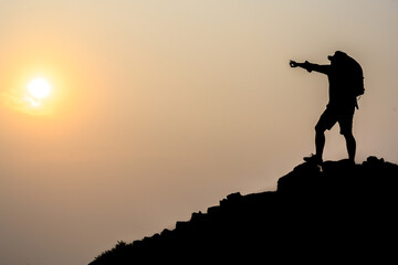 Silhouette of young male tourists Stand and watch the beautiful sunset on top of the mountain with your backpack.